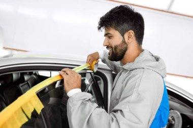 mechanic man with yellow paper tape plasters car for polishing it clipart