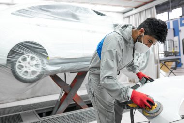 Genç oto tamircisi arabayı cilalıyor ve parlatıyor.