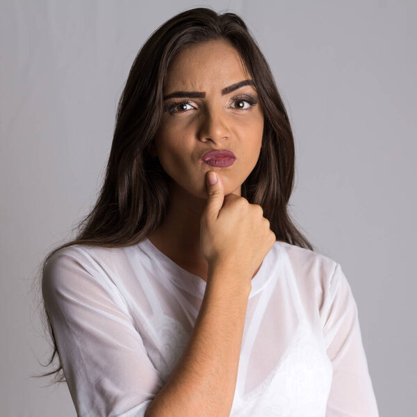 Portrait of Young Brazilian woman with long hair making grimace and looking at camera with serious expression.