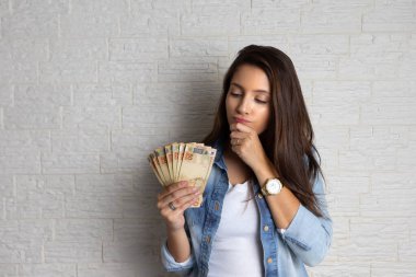 Genç ve güzel bir bayan Brezilya para birimine bakıyor. Finansal, kar, kredi, maliyet, satın alma, zengin konsept.