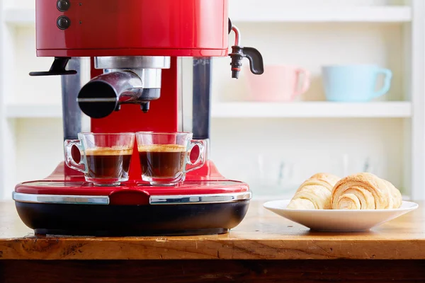 Two cups of espresso on espresso machine with croissants on plate
