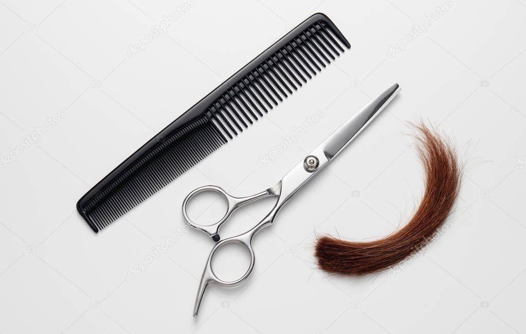 Hairdressers scissors with comb and lock of hair on white background