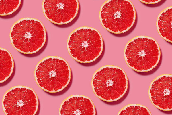Colorful fruit pattern of fresh grapefruit slices on pink background. Minimal flat lay concept.