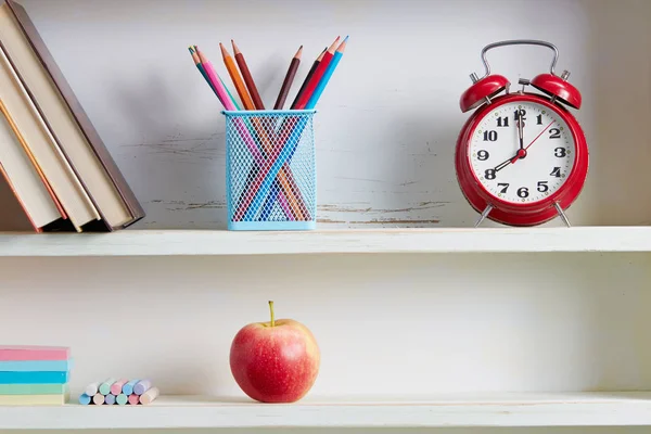Reloj despertador y útiles escolares en estante —  Fotos de Stock