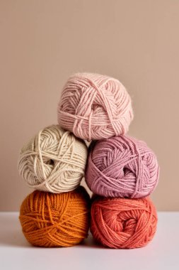 Renkli iplik yumakları pastel renkte ve tarafsız arkaplanda yığılmış sıcak tonlarda.