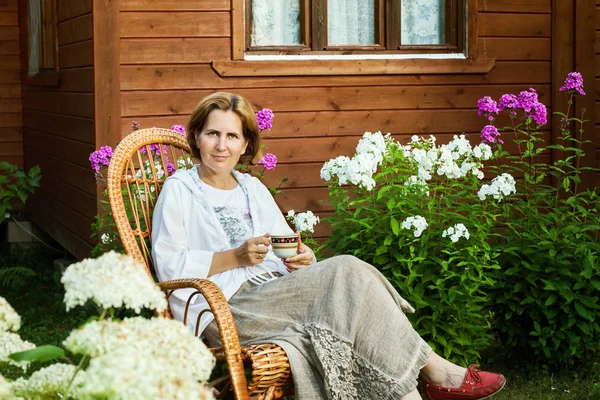 Smiling woman resting in wicker chair at summer cottage in evening