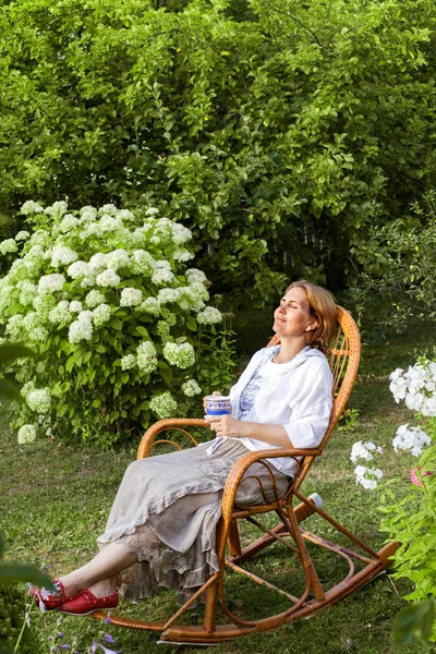 Smiling woman resting in wicker chair at summer cottage in evening