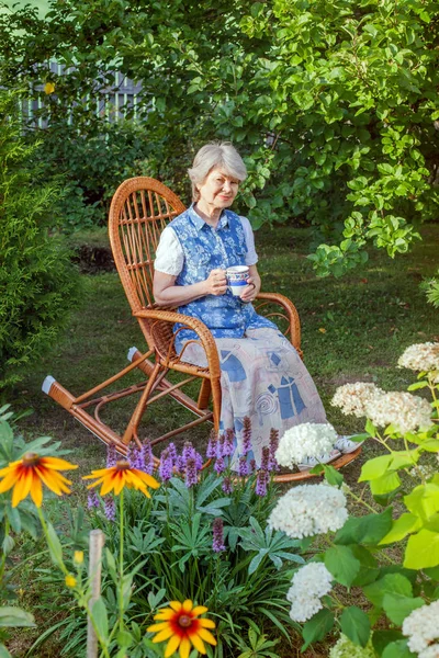 一杯茶的资深妇女休息在柳条椅在乡间别墅 — 图库照片