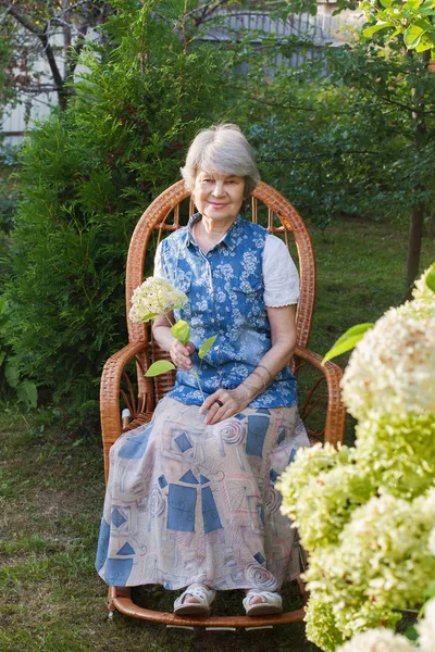 Alte Frau Ruht Schaukelstuhl Neben Blumenbeet — Stockfoto