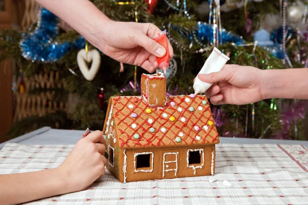 Hands of family painting gingerbread house with icing.