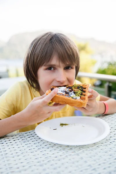 通りのカフェでワッフルを食べる少年が — ストック写真