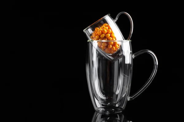 Sandthorn berries in a transparent mug on a black background — Stock Photo, Image