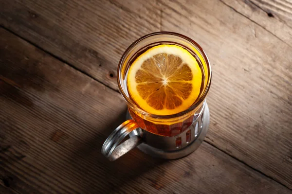 Чай с лимоном в стакане с держателем чашки на деревянном фоне на черном фоне — стоковое фото