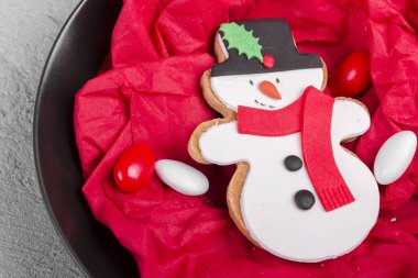 Lezzetli fırında Noel kurabiyesi siyah plaka üzerinde kardan adam şeklinde rustik ve hasarlı gri beton zemin üzerine izole kırmızı peçete Çerezler ile. Kurabiye pişmiş ya da küçük ve düz pişmiş gıda.