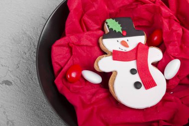 Lezzetli fırında Noel kurabiyesi siyah plaka üzerinde kardan adam şeklinde rustik ve hasarlı gri beton zemin üzerine izole kırmızı peçete Çerezler ile. Kurabiye pişmiş ya da küçük ve düz pişmiş gıda.