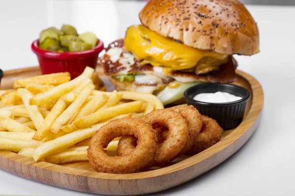 close up of burger with meat, cheese, vegetables, egg served with french fries and fry onion circles