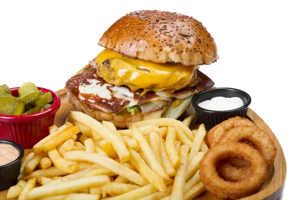 close up of burger with meat, cheese, vegetables, egg served with french fries and fry onion circles