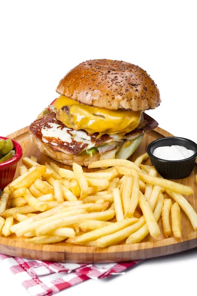 close up of burger with meat, cheese, vegetables and egg served with french fries and sauces