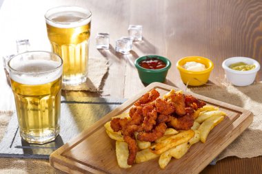 Soğuk köpüklü altın soğutulmuş taslak bira hizmet plakalı lezzetli sıcak gevrek ev yapımı taze kızarmış tavuk kanatları, dilimlenmiş domuz sosisi ve kişiler üzerine ahşap bambu tahta baharatlı sos ile.