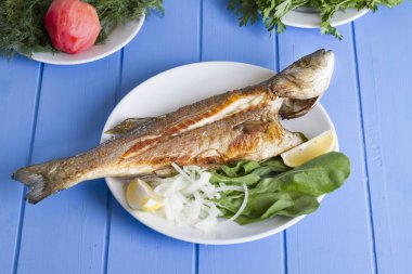 Yeşil ve mavi ahşap masa, deniz ürünleri kavramı üzerinde limon ile ızgara levrek balık