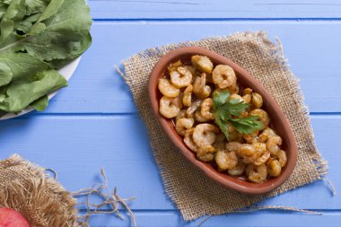 Lezzetli küçük kırmızı karides tereyağı ile baharat baharat haşlanmış. Geleneksel Yunan çanak çömlek içinde hizmet veren karides güveç. Üstten görünüm mavi rustik arka plan. En ortak gıda alerjenleri arasında diğer kabuklu deniz ürünleri.