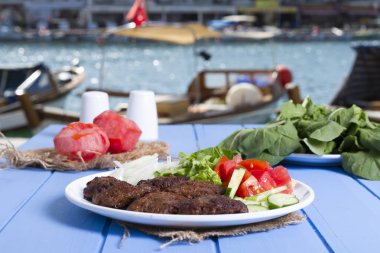 Izgara sığır eti köfte porsiyon dilimlenmiş salatalık, beyaz soğan, küp daire plakalı domates ve marul salatası mavi rustik ahşap masanın üstüne kesmek. Ekmek kırıntıları, tereyağı ve baharat gibi maddeler.