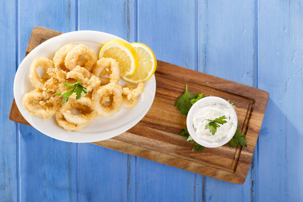 Delicious seafood golden fried crispy calamari rings at white plate with olive oil 