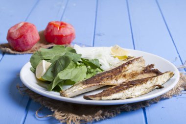 Lezzetli ızgara fileto levrek porsiyon dilimlenmiş soğan, domates, yeşil roka salatası ve sulu limon rustik mavi ahşap masa arka plan üzerinde oval beyaz plakalı füme. Alan, kopyalama kimse.