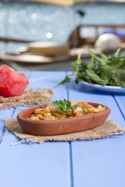 Lezzetli küçük kırmızı karides tereyağı ile baharat baharat haşlanmış. Geleneksel Yunan çanak çömlek içinde hizmet veren karides güveç. Üstten görünüm mavi rustik arka plan. En ortak gıda alerjenleri arasında diğer kabuklu deniz ürünleri.