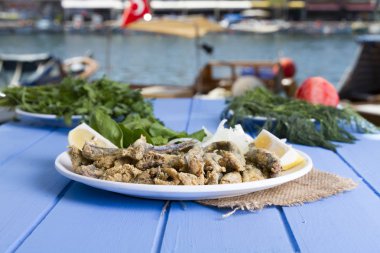 Tabak kızarmış taze mevsimlik otlar, hafif mavi ahşap masa dilimlenmiş soğan, roka, maydanoz ve limon ile hizmet veren kırmızı kefal balık. Mullus subtropikal deniz aile Levreksiler balık cinsidir.