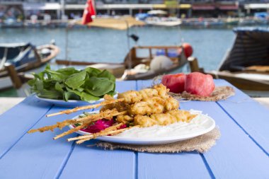 Lezzetli altın derin kızarmış pirzola midye yoğurt sos tartar ile hizmet veren şişleri, domates, dilimlenmiş beyaz soğan, maydanoz ve yeşil roka salatası mavi rustik masa arka plan üzerinde. Midye tava.