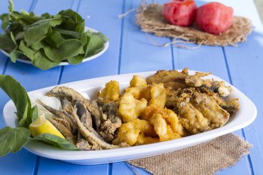 Lezzetli derin kızarmış Mix deniz ürünleri balık plaka mezgit, hamsi, sardalya, mavi rustik ahşap arka plan üzerinde beyaz soğan, limon, domates, roka salatası dilimlenmiş.