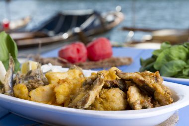 Lezzetli derin kızarmış Mix deniz ürünleri balık plaka mezgit, hamsi, sardalya, mavi rustik ahşap arka plan üzerinde beyaz soğan, limon, domates, roka salatası dilimlenmiş.