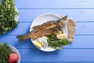 Yeşiller ve limon ile ızgara levrek balık üstten görünüm mavi ahşap tablo