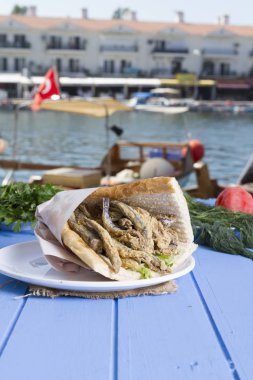 Türk geleneksel Delicious derin kurutulmuş Avrupa Hamsili balık malzemeleri yuvarlak tabak, mavi rustik arka plan masaya dilimlenmiş domates, roka salatası, beyaz soğan ve limon hizmet sandviç. Kopya alanı