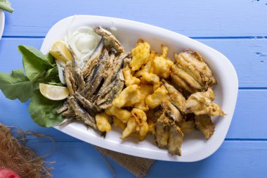 Lezzetli derin kızarmış Mix deniz ürünleri balık plaka mezgit, hamsi, sardalya, mavi rustik ahşap arka plan üzerinde beyaz soğan, limon, domates, roka salatası dilimlenmiş.