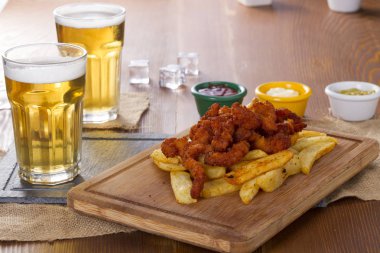 Soğuk köpüklü altın soğutulmuş taslak bira hizmet plakalı lezzetli sıcak gevrek ev yapımı taze kızarmış tavuk kanatları, dilimlenmiş domuz sosisi ve kişiler üzerine ahşap bambu tahta baharatlı sos ile.