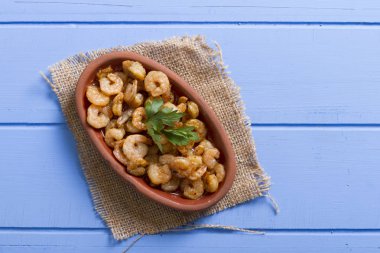 Lezzetli küçük kırmızı karides tereyağı ile baharat baharat haşlanmış. Geleneksel Yunan çanak çömlek içinde hizmet veren karides güveç. Üstten görünüm mavi rustik arka plan. En ortak gıda alerjenleri arasında diğer kabuklu deniz ürünleri.