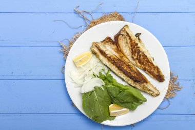 Lezzetli ızgara fileto levrek porsiyon dilimlenmiş soğan, domates, yeşil roka salatası ve sulu limon rustik mavi ahşap masa arka plan üzerinde oval beyaz plakalı füme. Alan, kopyalama kimse.