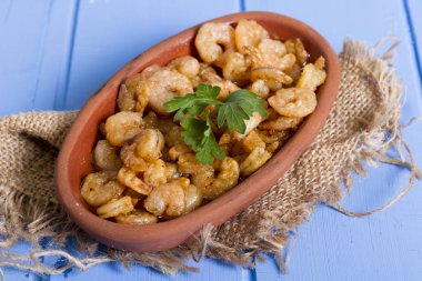 Lezzetli küçük kırmızı karides tereyağı ile baharat baharat haşlanmış. Geleneksel Yunan çanak çömlek içinde hizmet veren karides güveç. Üstten görünüm mavi rustik arka plan. En ortak gıda alerjenleri arasında diğer kabuklu deniz ürünleri.