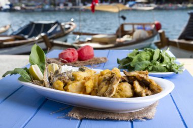 Lezzetli derin kızarmış Mix deniz ürünleri balık plaka mezgit, hamsi, sardalya, mavi rustik ahşap arka plan üzerinde beyaz soğan, limon, domates, roka salatası dilimlenmiş.