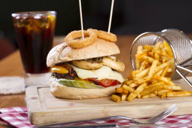 Ev yapımı hamburger marul, soğan, mantar, domates dilimleri, turşu, pastırma ve kaşar peynir porsiyon kızarmış baharatlı patates kızartması ile ahşap masa arka plan üzerinde.