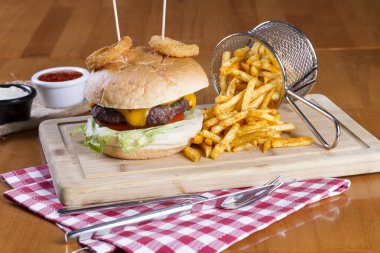 Ev yapımı hamburger marul, soğan, mantar, domates dilimleri, turşu, pastırma ve kaşar peynir porsiyon kızarmış baharatlı patates kızartması ile ahşap masa arka plan üzerinde.
