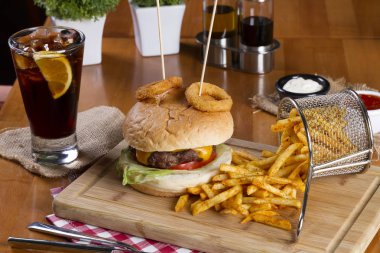 Ev yapımı hamburger marul, soğan, mantar, domates dilimleri, turşu, pastırma ve kaşar peynir porsiyon kızarmış baharatlı patates kızartması ile ahşap masa arka plan üzerinde.