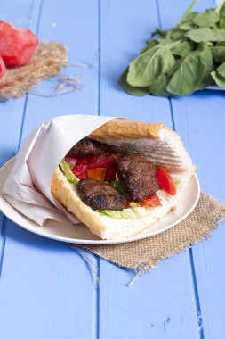 Lezzetli Türk köfte sandviç, Köfte Ekmek. Maddeler ile ekmek kırıntısı, tereyağı, soğan, salatalık, domates, marul salatası, turşu ve baharat baharat dilimlenmiş. Mavi masaya hizmet hamburger.