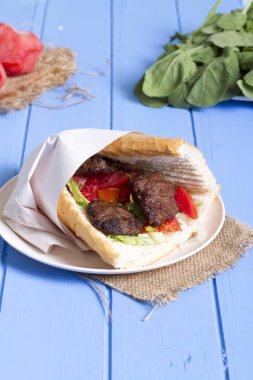 Delicious Turkish Meatballs Sandwich, Kofte Ekmek. Ingredients with bread crumbs, butter, sliced onion, cucumber, tomato, lettuce salad, pickles and seasoning spices. Hamburger serving on blue table. clipart