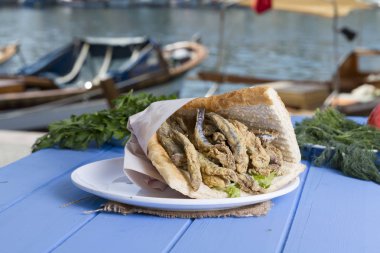 Türk geleneksel Delicious derin kurutulmuş Avrupa Hamsili balık malzemeleri yuvarlak tabak, mavi rustik arka plan masaya dilimlenmiş domates, roka salatası, beyaz soğan ve limon hizmet sandviç. Kopya alanı