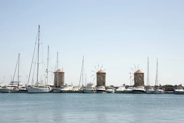 Three beautiful ancient stone Windmills in the Mandraki port with some cruise boats at Rhodes, Greece. Behind on the left you can see the cassel of the old medieval town.