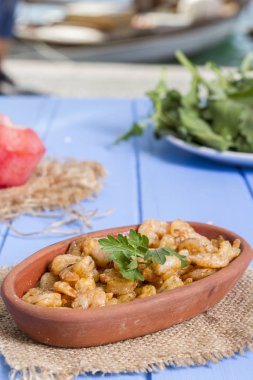 Lezzetli küçük kırmızı karides tereyağı ile baharat baharat haşlanmış. Geleneksel Yunan çanak çömlek içinde hizmet veren karides güveç. Üstten görünüm mavi rustik arka plan. En ortak gıda alerjenleri arasında diğer kabuklu deniz ürünleri.