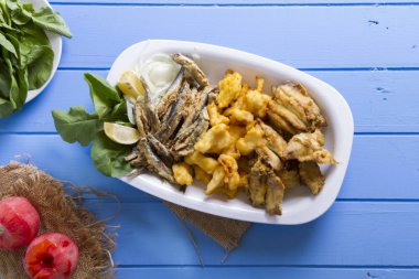 Lezzetli derin kızarmış Mix deniz ürünleri balık plaka mezgit, hamsi, sardalya, mavi rustik ahşap arka plan üzerinde beyaz soğan, limon, domates, roka salatası dilimlenmiş.